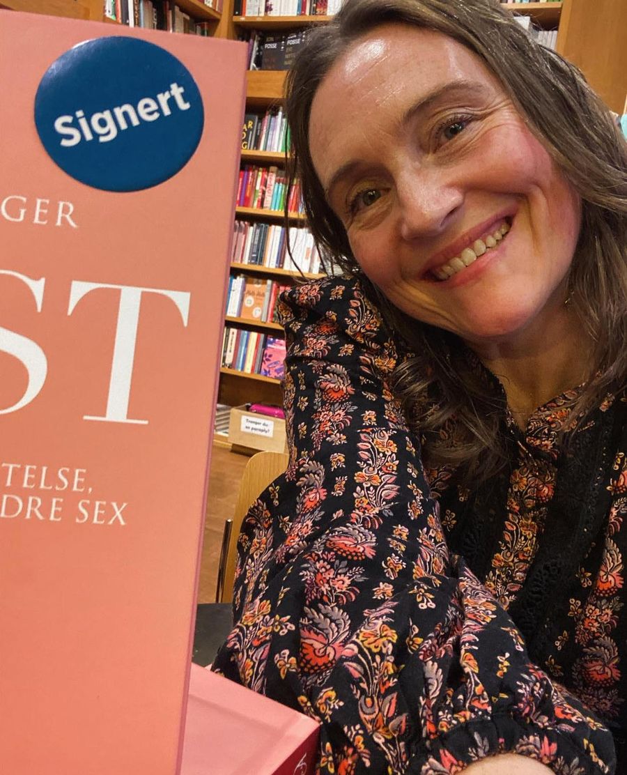 Elin Enger smiler ved siden av en stabel med boken LYST i en bokhandel
